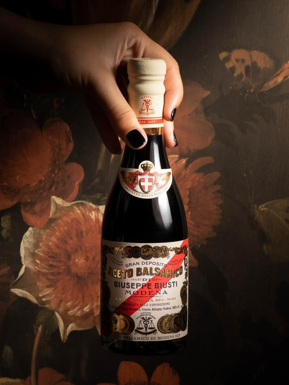A hand holding a bottle of Giuseppe Giusti balsamic vinegar against a floral background